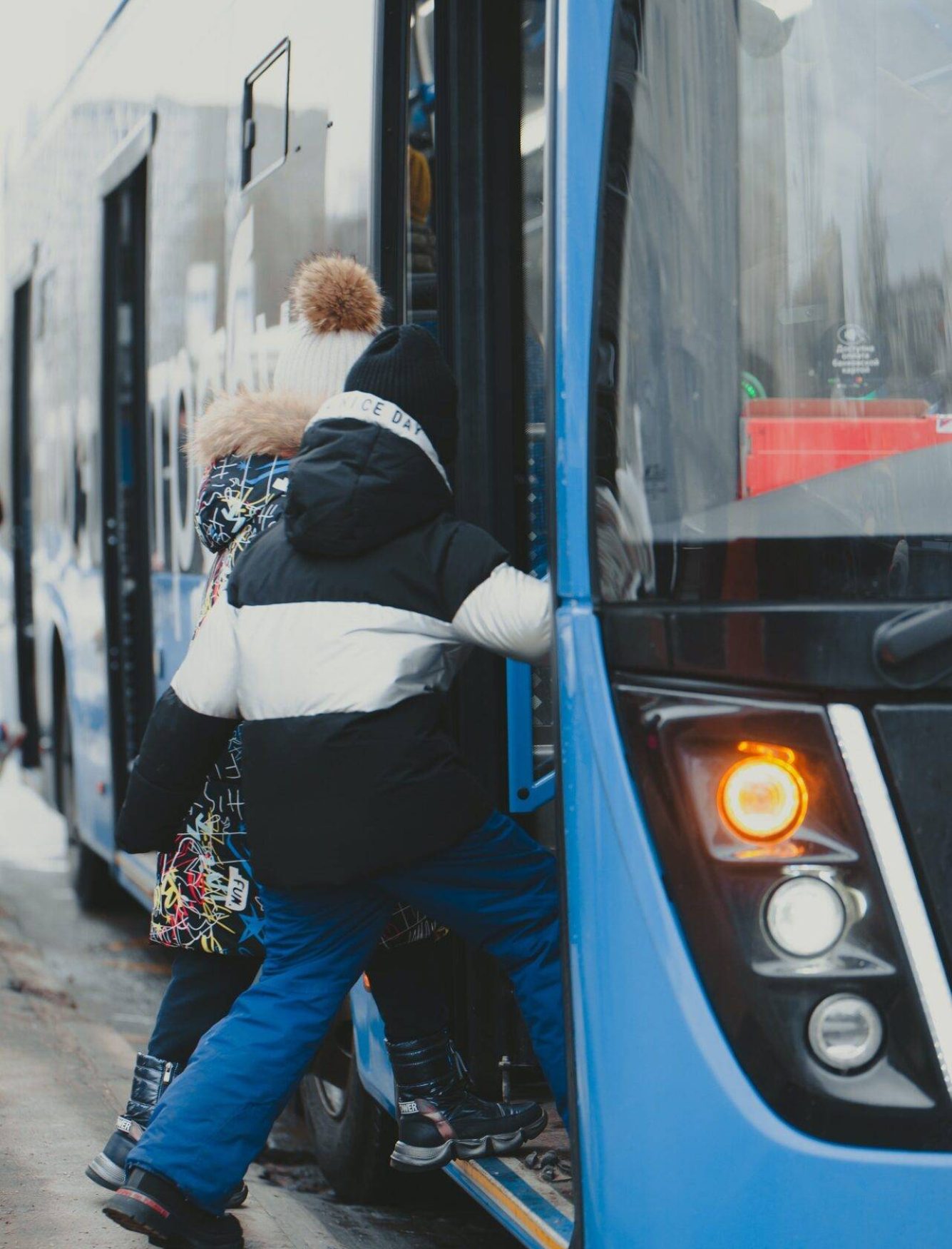 the-girls-enter-the-doors-of-a-blue-bus-that-has-arrived-at-the-bus-stop-.jpg